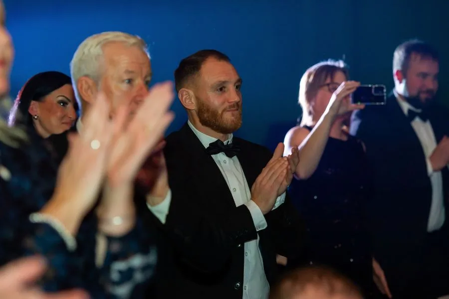 Guests in evening dress applaud at the Ashford Hero Awards while one films on a phone